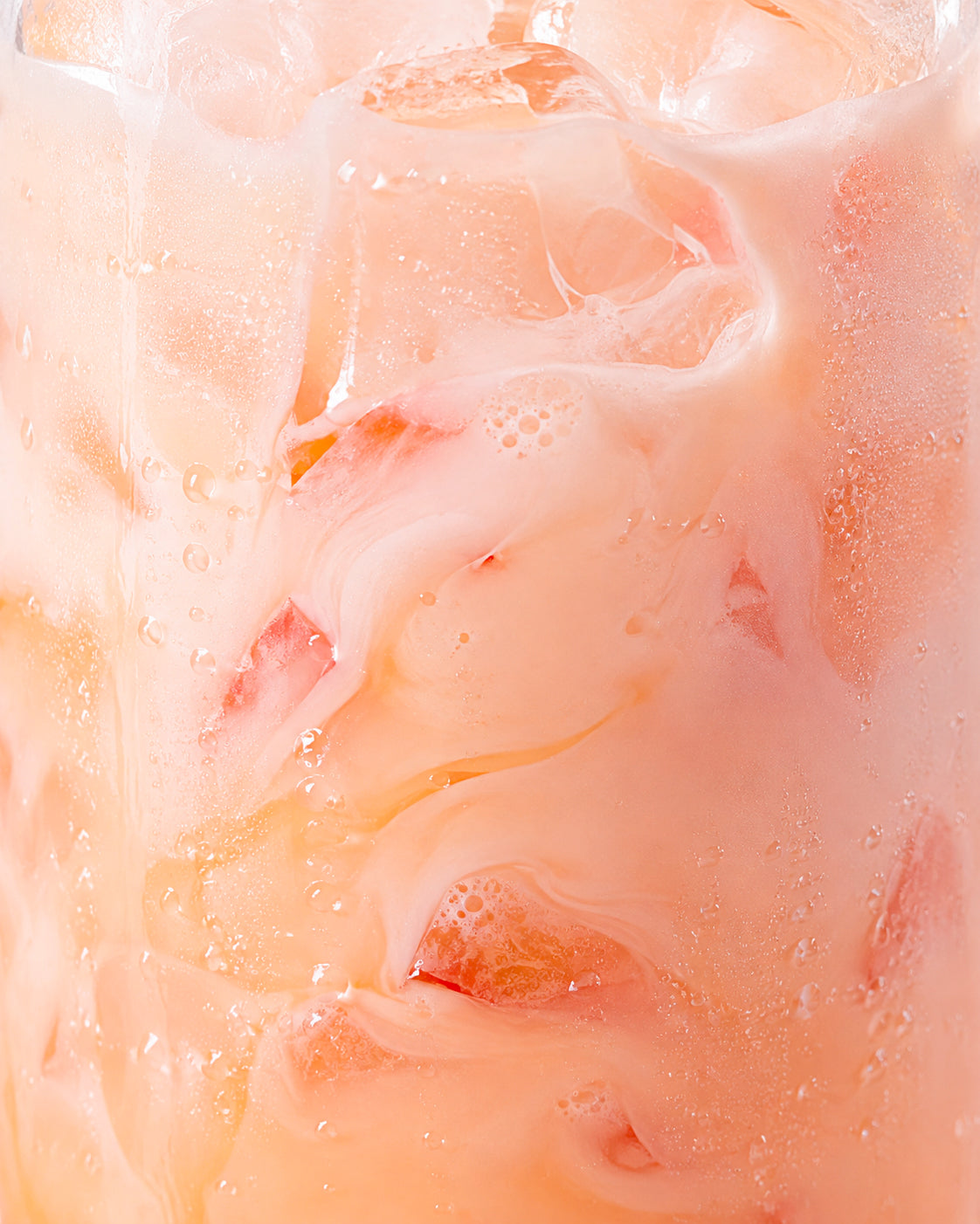 A close-up of a pale pink iced drink with ice cubes and visible condensation droplets.