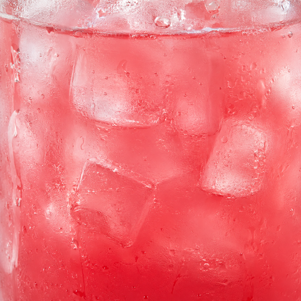 A close-up of a pink-red iced drink in a clear glass, filled with large ice cubes and covered in condensation droplets.