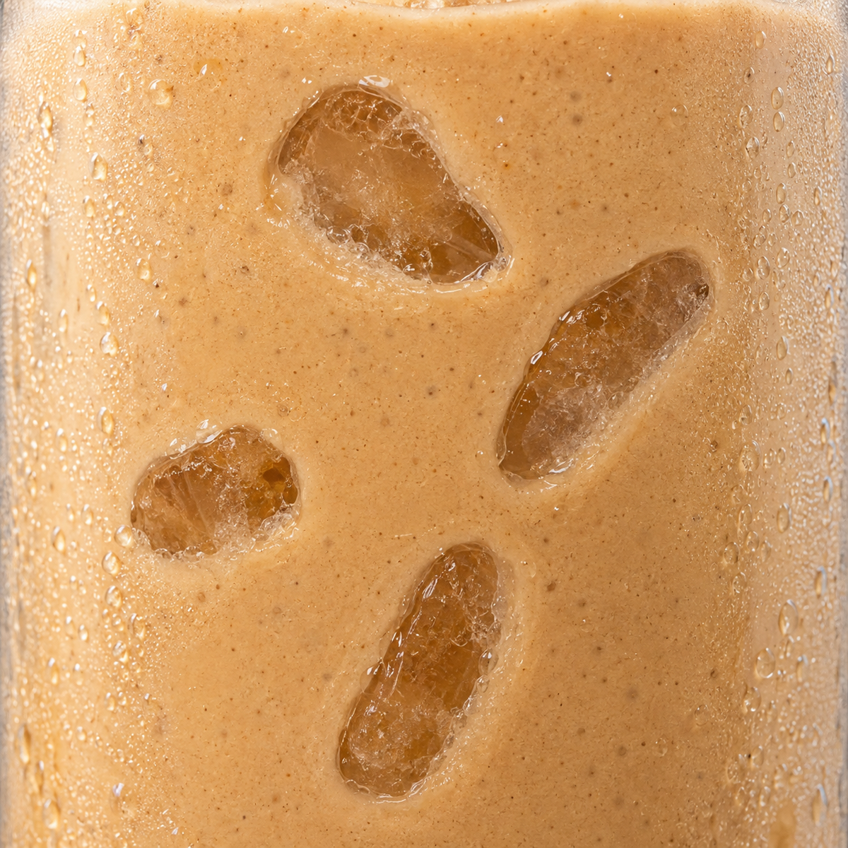 A close-up of a frothy light brown beverage with ice cubes visible through the surface, covered in condensation droplets.