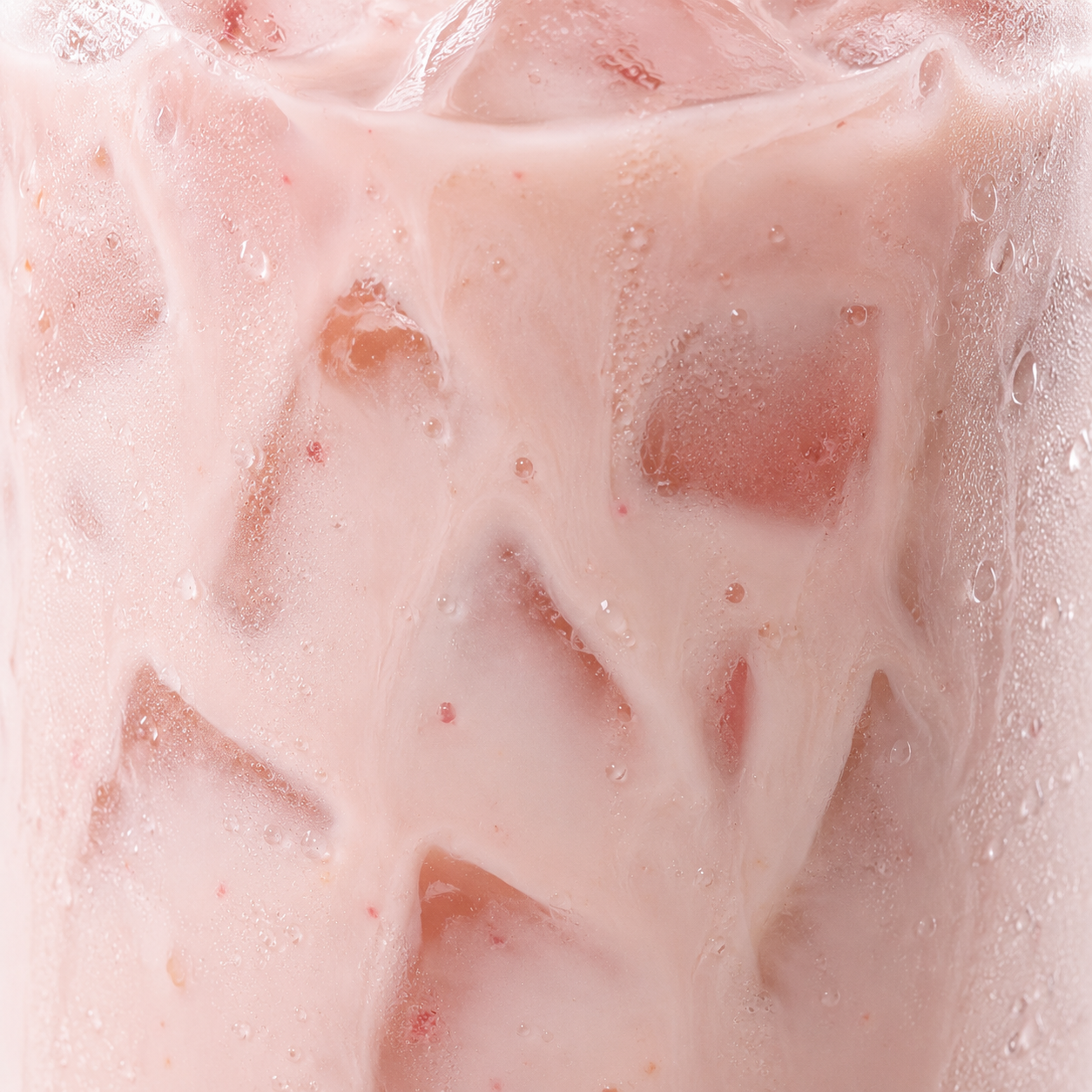 A close-up of a frosted glass filled with a pale pink iced drink, showing ice cubes, condensation droplets, and a light pink color throughout.